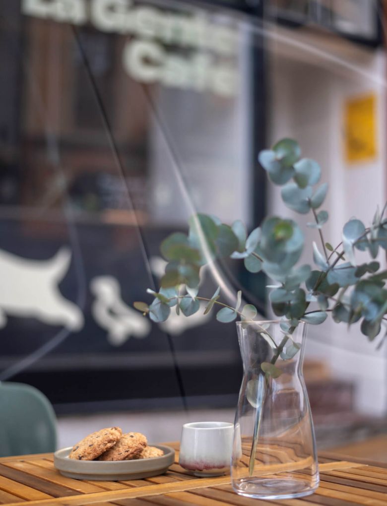 A table at La Gente Cafe features a vase of flowers and a plate of cookies, designed by TenZeroTwo Bureau