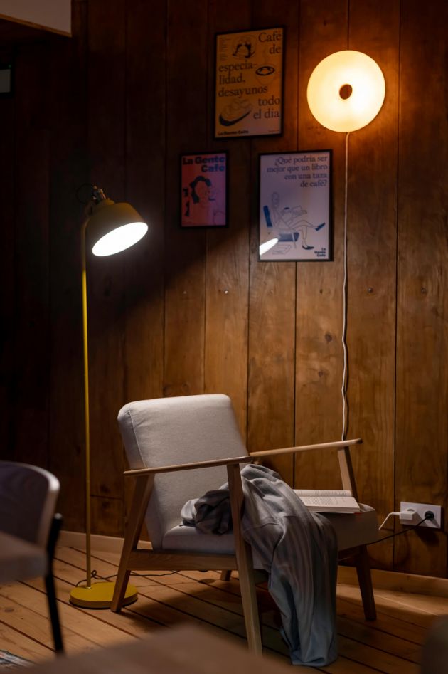 A cozy room featuring a chair and a lamp against warm wooden walls